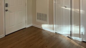 Um corredor com duas portas brancas, uma delas com uma grelha de ventilação, e chão de madeira.