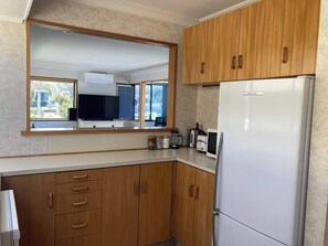 A kitchen with wooden cabinets, a white refrigerator, a coffee maker, and a toaster. - Retro Charm in the Mount (Mount Maunganui)