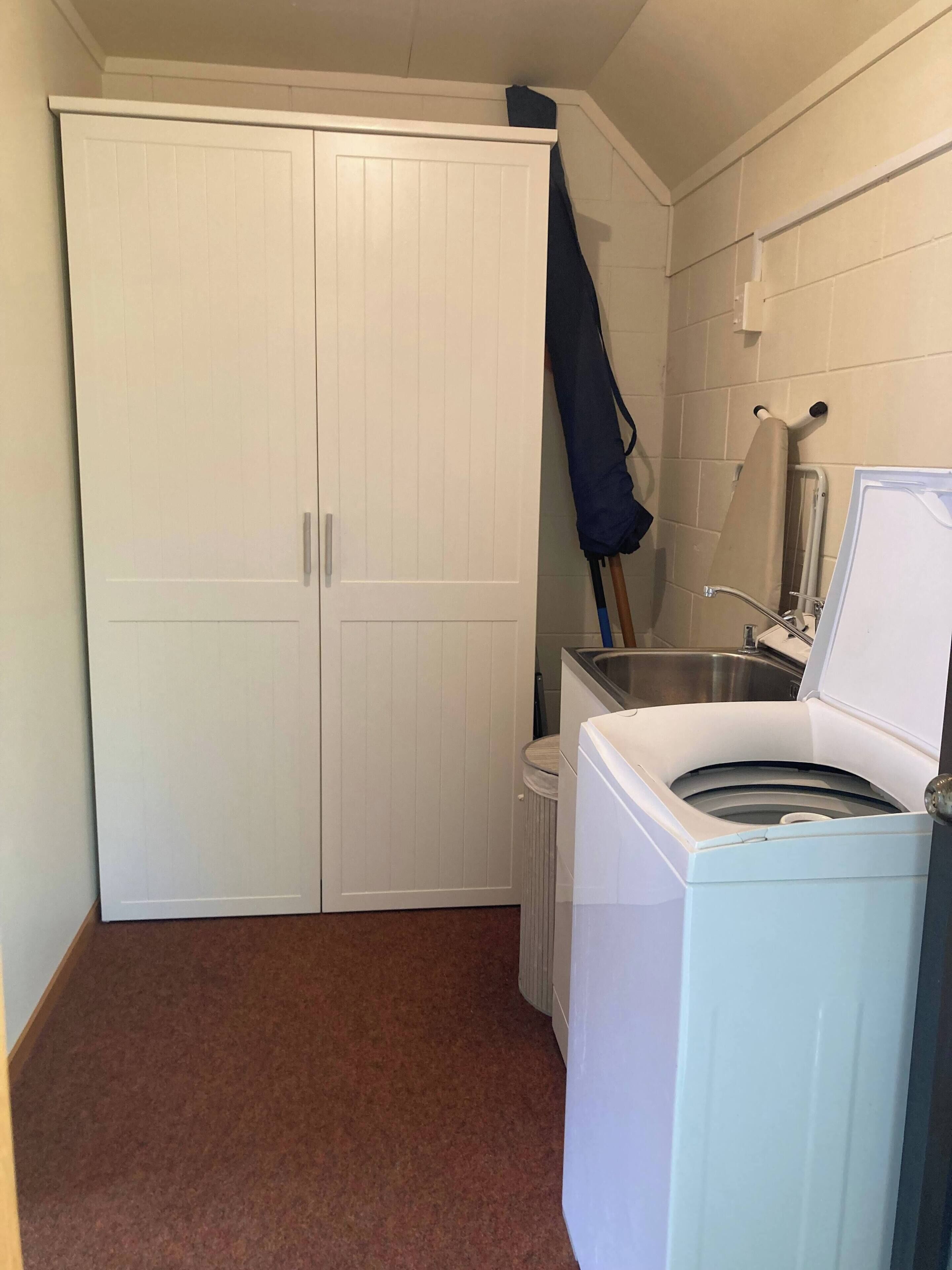 A laundry room with a white washing machine, a drying rack, and a white wardrobe.