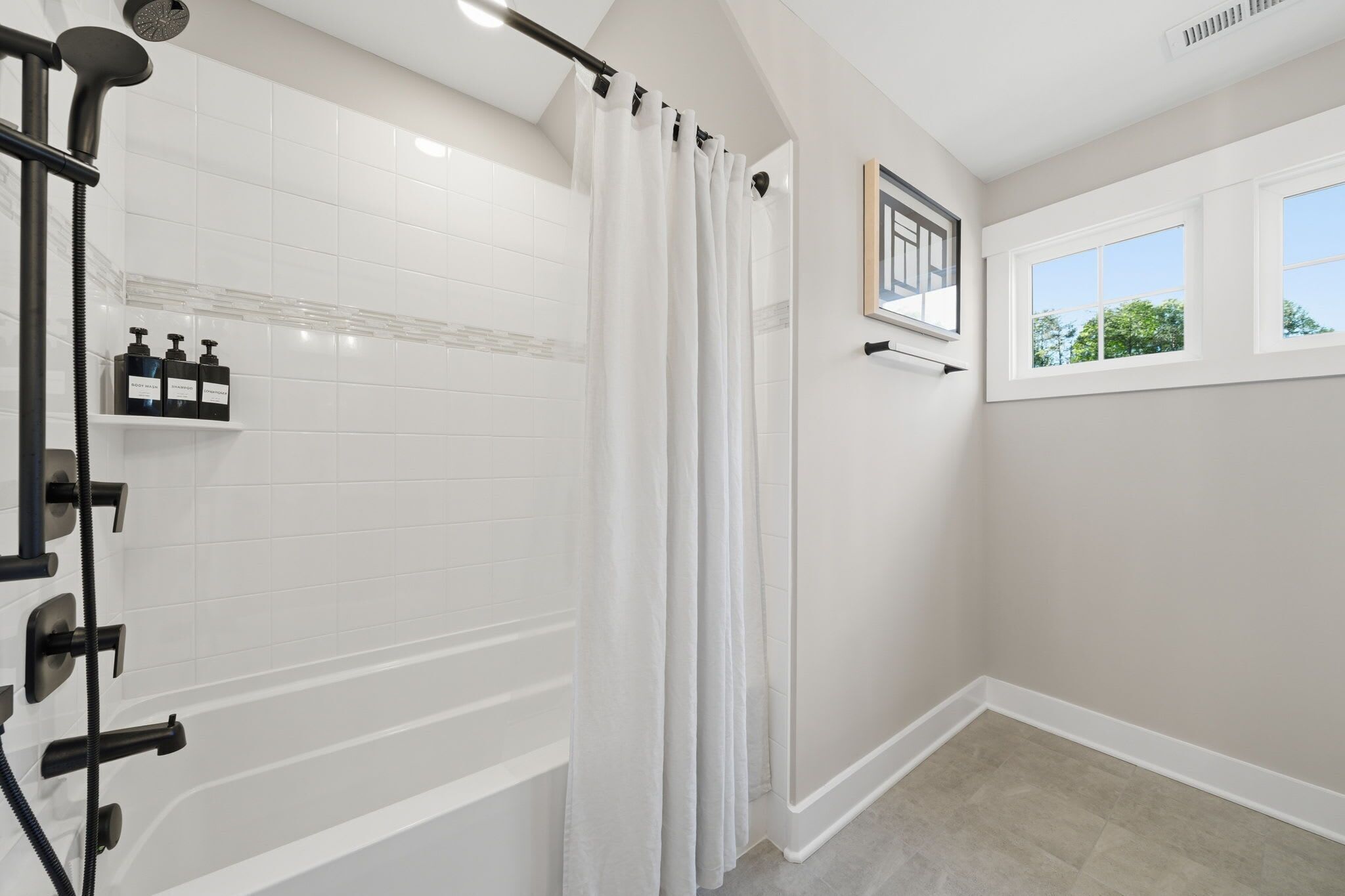 A modern bathroom with a walk-in shower, white tiled walls, a window with a view, and a shelf with toiletries.