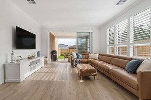 A modern living room with a large flat-screen TV, a brown leather sofa, a white console table, and a sliding glass door leading to an outdoor area. - Beachurst Coastal Escape | Walk to Beach (Dromana)