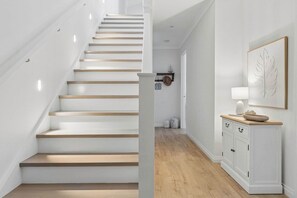 A staircase with wooden steps and white walls, a white cabinet with drawers, and a framed leaf artwork on the wall. - Saltwater Sanctuary | Walk to Beach (Dromana)