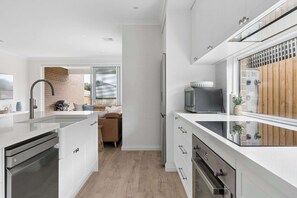 A modern kitchen with white cabinetry, stainless steel appliances, and a glass backsplash. - Beachurst Coastal Escape | Walk to Beach (Dromana)