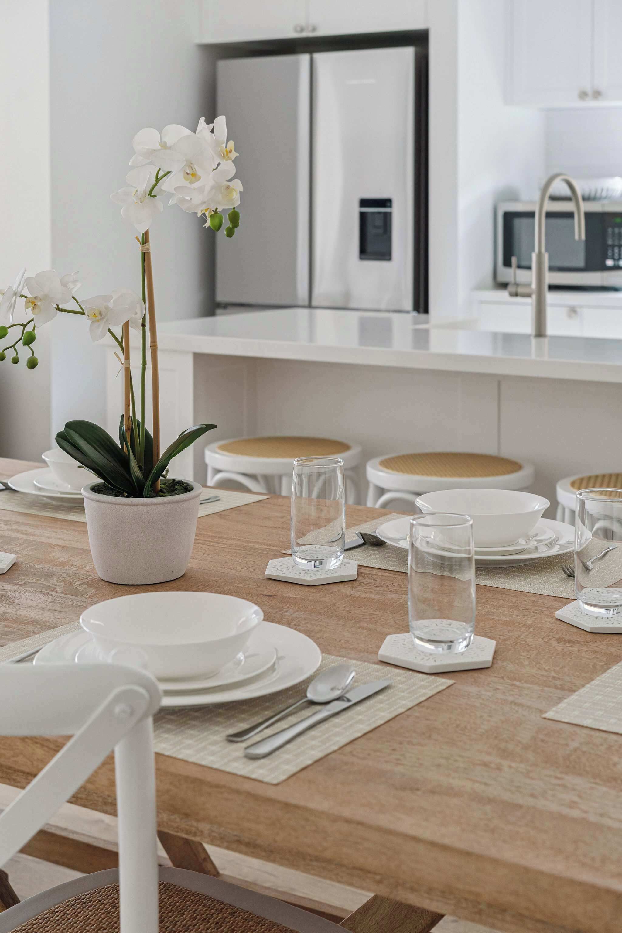 A modern kitchen with white appliances, a dining table set with white plates and glasses, and a potted orchid.