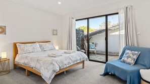 Ein Schlafzimmer mit Bett, Sessel, Tisch und Blick ins Freie.