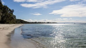 A beach with clear water, a sandy shore, and a distant sailboat.