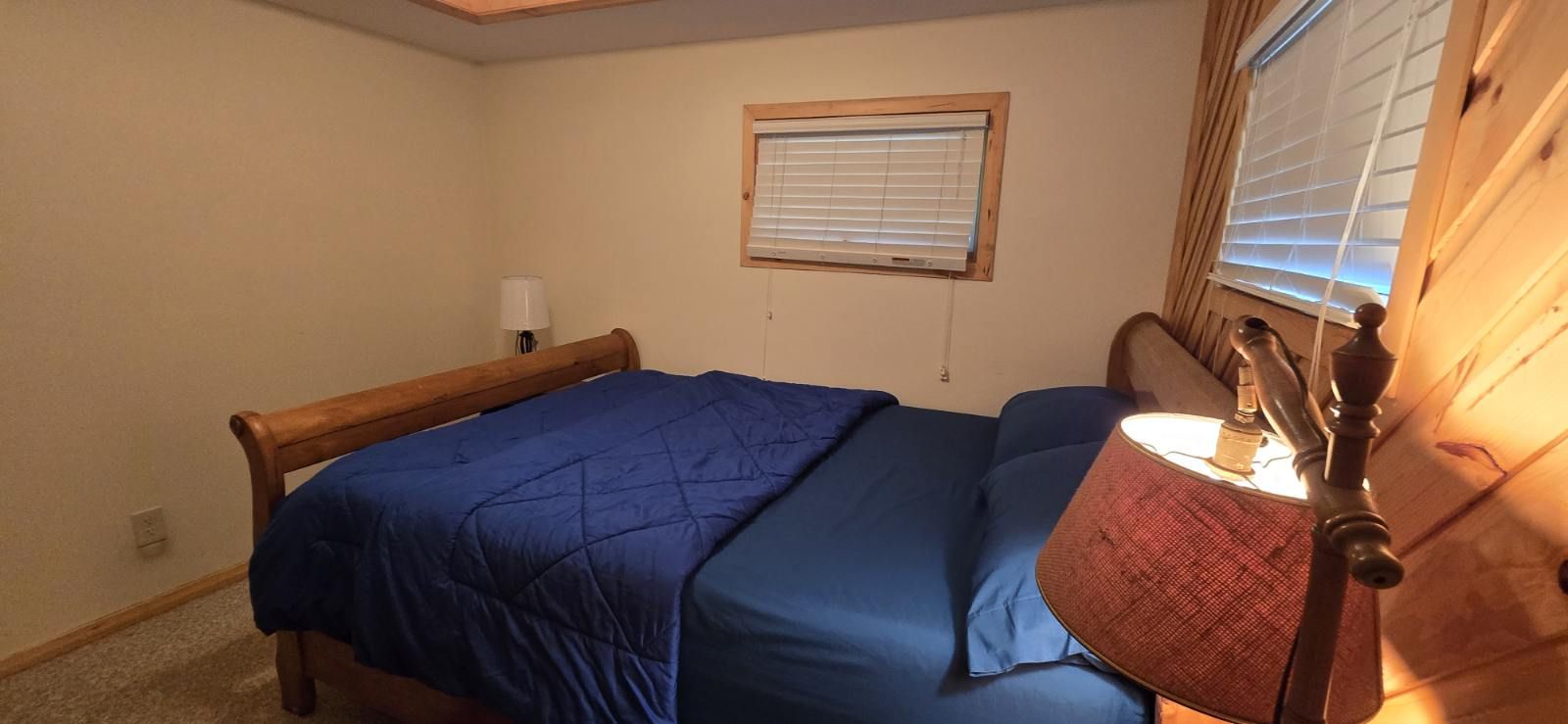Ein Schlafzimmer mit einem Bett, einem Nachttisch, einer Lampe und einem Fenster mit Jalousien.