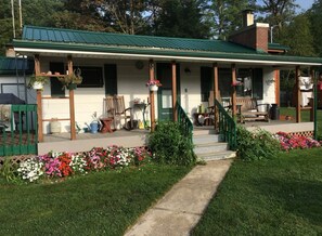 A house with a porch, a front door, and a small garden with flowers. - Clear Lake Retreat • Big Deck • Fire Pit • Views (Tionesta)