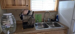 A kitchen with a double sink, a dish rack, a water dispenser, and wooden cabinets. - Clear Lake Retreat • Big Deck • Fire Pit • Views (Tionesta)