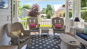 Une véranda couverte avec des meubles en osier, un tapis à motifs et une vue sur les maisons au loin.