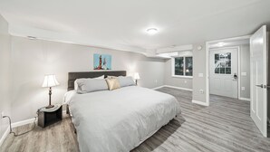 A modern bedroom with a large bed, two bedside tables, a nightstand, a painting on the wall, and a door leading to another room. - Charming 6-Bedroom Accessible Retreat Near Downtown Stillwater - Daffodil House (Stillwater)