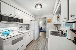 A modern kitchen with white cabinets, a stainless steel range, a blue kettle, and a built-in microwave.