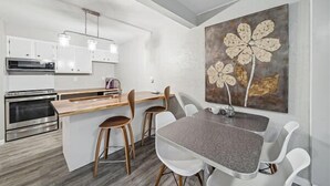 A modern kitchen with white cabinets, a built-in oven, and a dining area with a grey table and white chairs. - Accessible 3-Bedroom Retreat Near Historic Downtown Stillwater - Morning Glory (Stillwater)