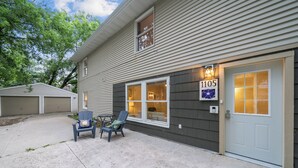 A two-story house with a garage, a front door with a number plaque, and two blue chairs outside. - Accessible 3-Bedroom Retreat Near Historic Downtown Stillwater - Morning Glory (Stillwater)