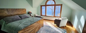 A bedroom with a large bed, a window with a view, a radiator, and a chair.