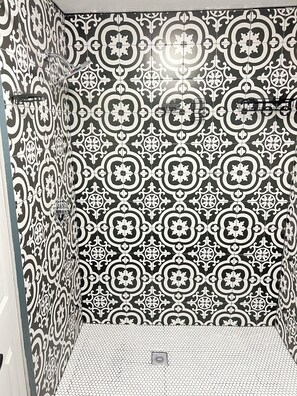 Une salle de bain avec des carreaux noirs et blancs formant un motif, un espace douche et un drain apparent.