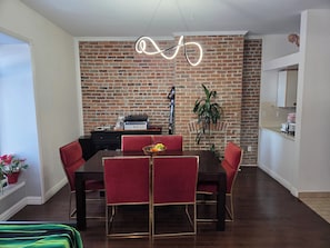 Un espace repas avec un mur en briques, un luminaire moderne et des chaises rouges.