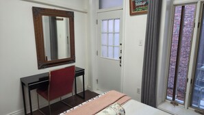 Une chambre à coucher comprenant un lit, un bureau, une chaise, un miroir, une fenêtre et une porte.