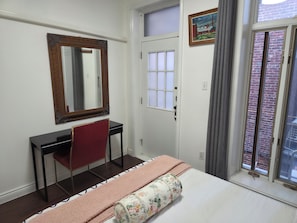 Une chambre à coucher comprenant un lit, un bureau, une chaise, un miroir, une fenêtre et une porte.