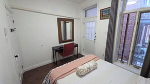 Une chambre à coucher avec un lit, un bureau, une chaise, un miroir, une fenêtre et une porte.