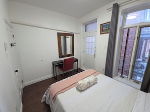 Une chambre à coucher avec un lit, un bureau, une chaise, un miroir, une fenêtre et une porte.