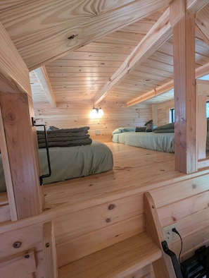 L’intérieur d’une cabane comprend un lit en mezzanine, un deuxième lit, un escalier et un luminaire fixé au mur.