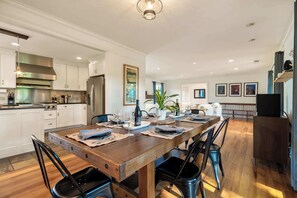 A modern kitchen with white cabinets, stainless steel appliances, and a wooden dining table set for six. - Oak and Stone | Pool + Glen Ellen Wine Country (Glen Ellen)
