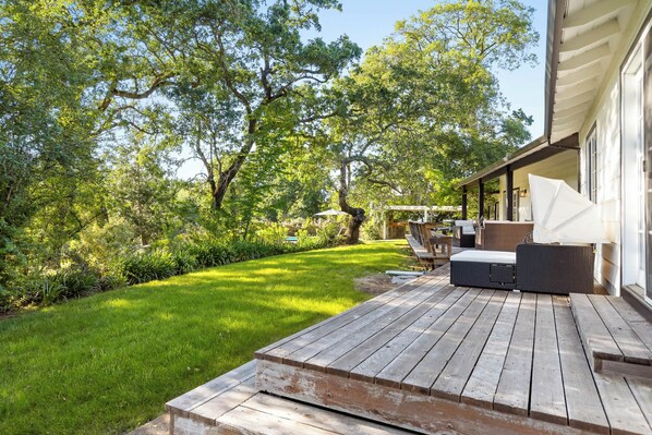 Une terrasse en bois avec des meubles d’extérieur, un espace salon couvert et une pelouse bien entretenue.