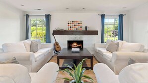 A living room with a fireplace, two white sofas, a coffee table, and a guitar. - Oak and Stone | Pool + Glen Ellen Wine Country (Glen Ellen)