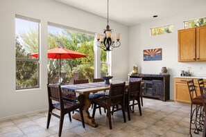 A dining area with a table, chairs, a chandelier, and a red umbrella. - Golf Course Desert Retreat with Private Patio (Scottsdale)