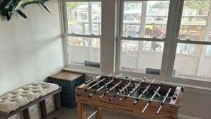 Habitació amb taula de futbolí, una banca amb coixins i grans finestres.