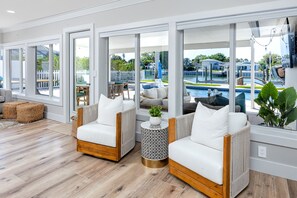 A spacious living area with large windows, two white cushioned sofas, a round side table, and a view of a pool and outdoor seating. - Luxury Water Front Entire Home Pool (St Petersburg)