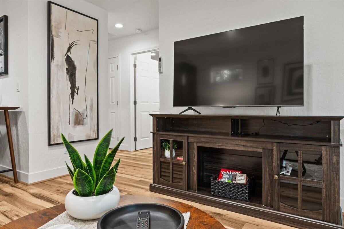Un salon avec un téléviseur à écran plat fixé à un meuble de télévision en bois foncé, une plante en pot et une télécommande posée sur une table en bois.