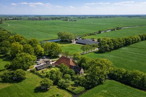 An aerial view of a rural property with a large field, a small building, and a house surrounded by trees. - Br Ndemar Boerderijkamer (Weidum)