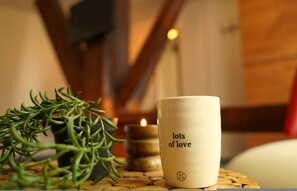A candle with 'lots of love' text, a potted plant, and a candle holder on a table. - Br Ndemar Boerderijkamer (Weidum)