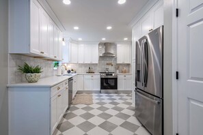 A kitchen with white cabinets, a stainless steel refrigerator, a gas stove, and a tiled floor.