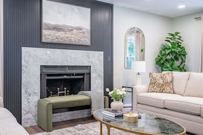 A living room with a fireplace, a sofa, a coffee table, and a large plant.