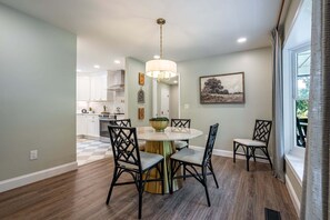 A dining area with a round table, four chairs, a chandelier, and a painting on the wall.