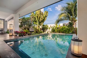 A modern pool area with a clear view of the sky, surrounded by lush tropical plants and a well-maintained patio.