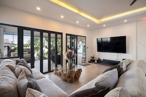 A modern living room with a large flat-screen TV, a glass coffee table, and a sofa. - Almara Boutique Villa - Private Spa Bang tao Beach (Choeng Thale)