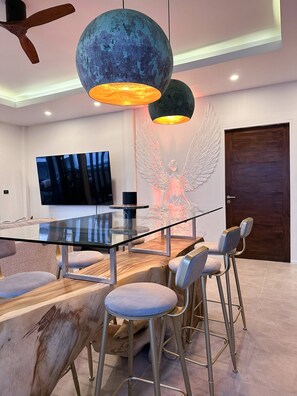 A modern dining area with a glass table, metal chairs, and a large TV.