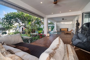A spacious living area with a wooden floor, a sofa, a chair, and a view of a lush garden.