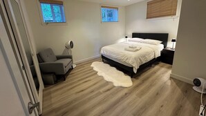 Een slaapkamer met een bed, nachtkastjes, een stoel, een ventilator en een raam.