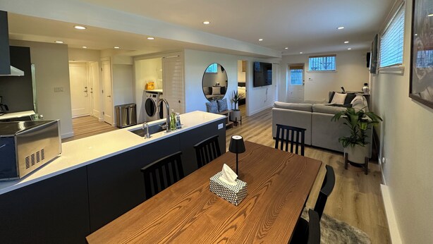 Een moderne keuken met een centraal eiland, een eethoek met een houten tafel en een woonkamer met een bank en een televisie.