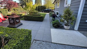 Een oprit met een pad naar een huis, omringd door verschillende planten en een lantaarnpaal.