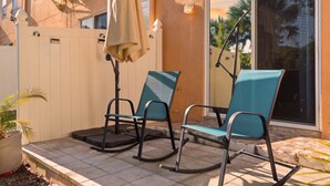 Een terras met twee schommelstoelen, een potplant en een witte hek.
