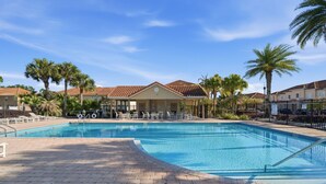 Una piscina con solárium empedrado, sillas de descanso y palmeras.
