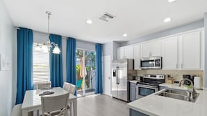 Una cocina moderna con armarios blancos, electrodomésticos de acero inoxidable y un comedor con mesa y sillas.