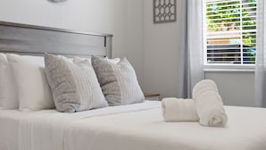 Una cama bien hecha con almohadas blancas y grises, un cabecero de madera y una ventana con persianas.