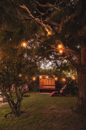 Ein Baumhaus mit einer Holzterrasse und Lichterketten, umgeben von Bäumen und Gras.